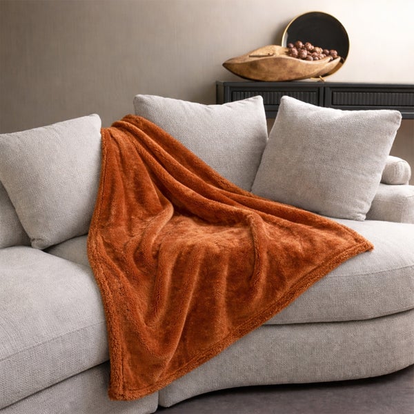 Weiche Kuscheldecke auf einem gepolsterten Sofa mit Dekokissen in einem wohnlichen Wohnbereich.