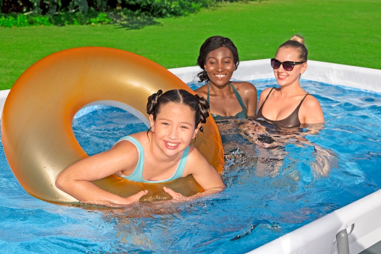 Mädchen mit aufblasbarem Schwimmring und zwei Frauen in einem rechteckigen Aufstellpool im Garten.