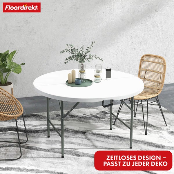 Floordirekt Logo. Runder weißer Klapptisch mit grauen Metallbeinen in hellem Raum. Zwei Rattanstühle stehen an dem Tisch auf einem Musterteppich.