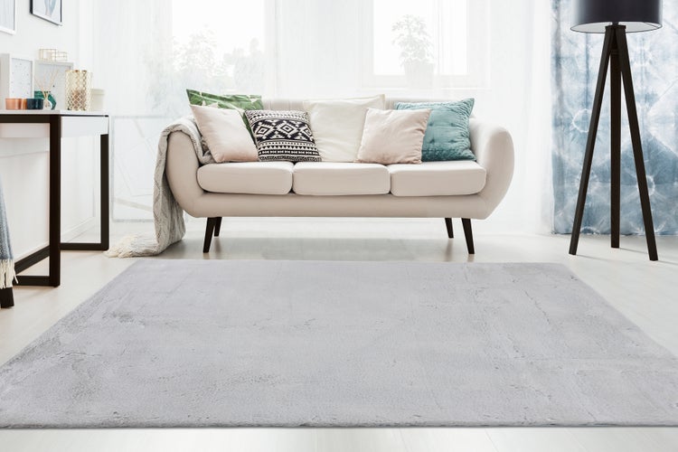 Heller Wohnraum mit gemütlichem Sofa, Dekokissen und weichem Teppich im Fokus.