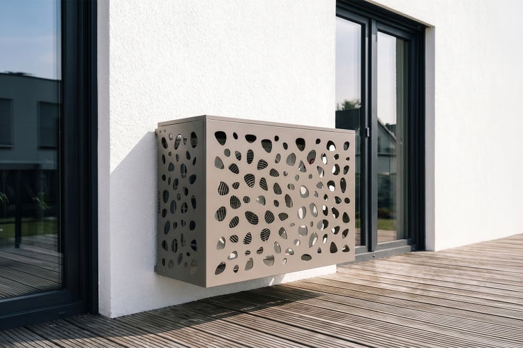 Klimaanlagen-Verkleidung aus Metall mit organischem Lochmuster, montiert an einer Hauswand über einer Holzterrasse im hellen Außenbereich.