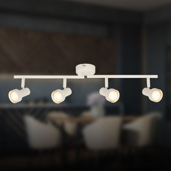 Weiße Deckenleuchte aus Metall mit vier verstellbaren Strahlern an einer geraden Schiene, leuchtend mit warmem Licht vor einem Wohnbereich.