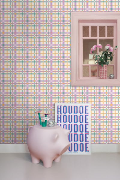 Tapete mit buntem Karomuster in einem hellen Zimmer mit Fensterrahmen, Schweinefigur und Plakat.