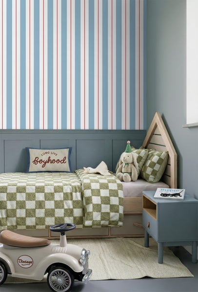 Kinderzimmer mit einer gestreiften Tapete an der Wand, einem hölzernen Hausbett, karierter Bettwäsche und dekorativen Spielzeugen.
