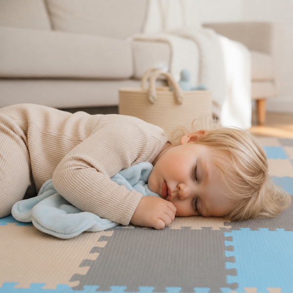 Kleinkind schläft friedlich auf einer gesteckten Puzzlematte aus Schaumstoff mit Kuscheldecke in einer hellen Wohnzimmerumgebung.