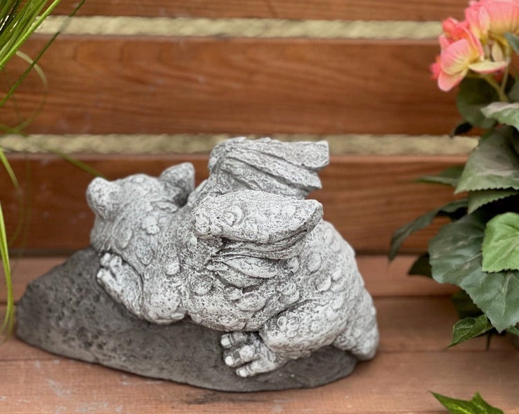 Gartenfigur in Form eines schlafenden Drachens aus Steinguss, auf einem Stein liegend