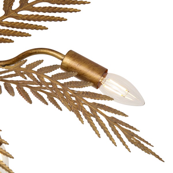 Detail einer goldfarbenen Wandleuchte aus Metall mit Farnblatt-Dekor und einer brennenden Kerzenlampe.