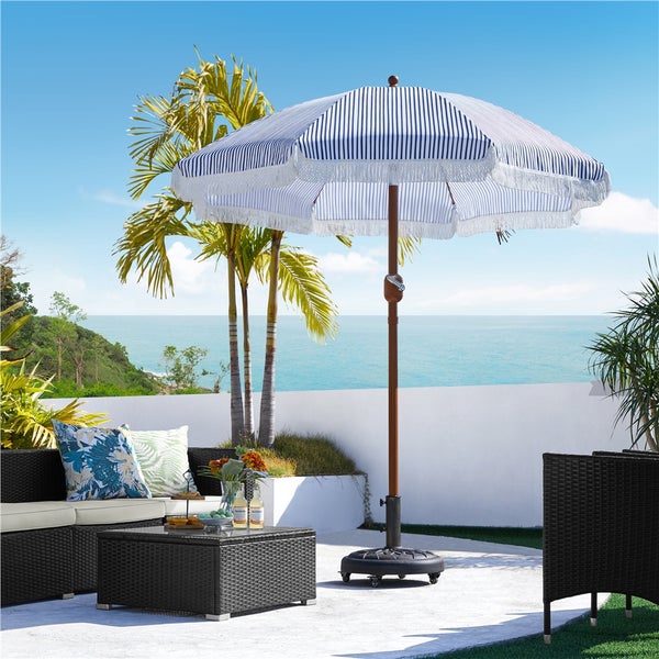 Gestreifter Gartenschirm mit Fransen und braunem Holzstiel steht auf einer Terrasse mit Rattanmöbeln.