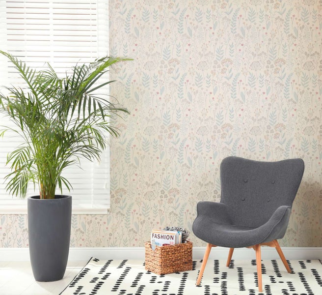 Vliestapete mit feinem floralem Wiesenmuster in einem hellen Wohnzimmer mit Sessel, Pflanze und Dekokorb vor der Wand.