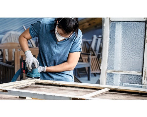 Frau schleift Fensterrahmen mit einem Schleifgerät