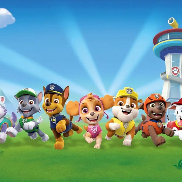 Paw Patrol Charaktere rennen über eine Wiese vor dem Lookout Hauptquartier und dem Himmel.