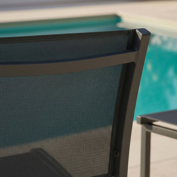 Detail der Rückenlehne eines Gartenstuhls aus dunklem Metall und Textilgewebe in einer hellen Außenanlage mit Schwimmbecken.