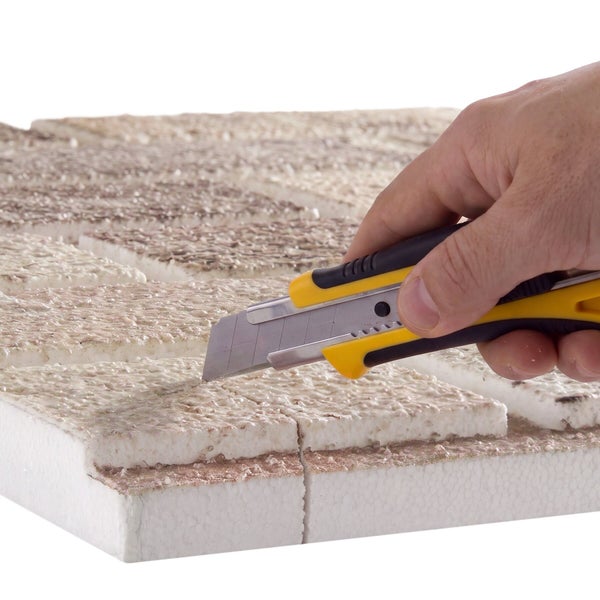 Hand die eine Styroporplatte mit einem Cuttermesser schneidet