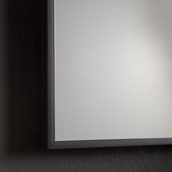 Nahaufnahme der Ecke eines Wandspiegels mit einem schmalen schwarzen Rahmen aus Aluminium.