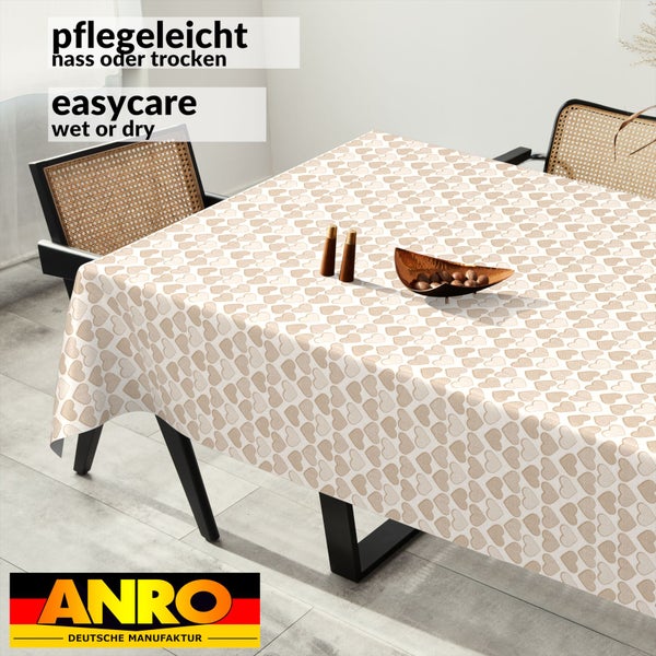 Pflegeleichte rechteckige Tischdecke mit Herz-Muster auf einem Tisch in einem hellen, modern eingerichteten Raum mit Stühlen in Geflecht-Optik.