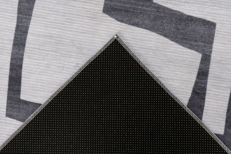 Detailaufnahme einer Teppichrückseite mit rutschfester Beschichtung und geketteltem Rand auf einem gemusterten Teppichobermaterial.