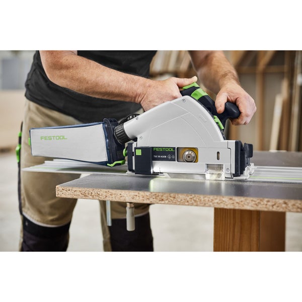 Festool Akku-Tauchsäge TSC 55 KSEB im Einsatz auf einer Führungsschiene mit Staubfangbeutel beim Sägen einer Holzplatte.
