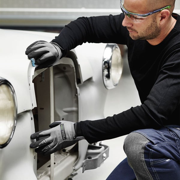 Ein Mann mit Schutzbrille und Arbeitshandschuhen arbeitet an einem weißen Auto.
