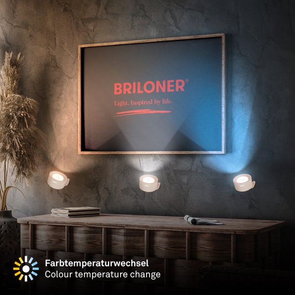 Drei kleine weiße LED-Wandstrahler mit Farbtemperaturwechsel von Warmweiß bis Kaltweiß beleuchten ein Bild an einer Wand. Briloner Logo.