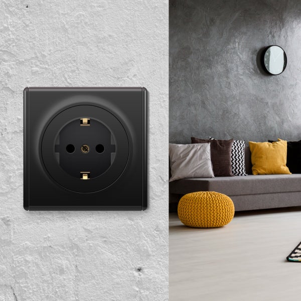 Moderne Steckdose in quadratischer Ausführung an einer weißen Wand, im Hintergrund ein modern eingerichtetes Wohnzimmer mit Sofa und Kissen.