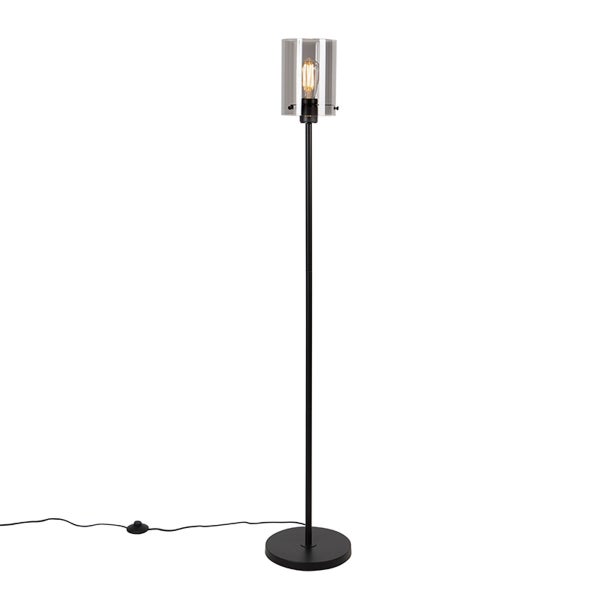 Stehleuchte aus schwarzem Metall mit zylindrischem Glasschirm, sichtbarem Leuchtmittel und Fußschalter.