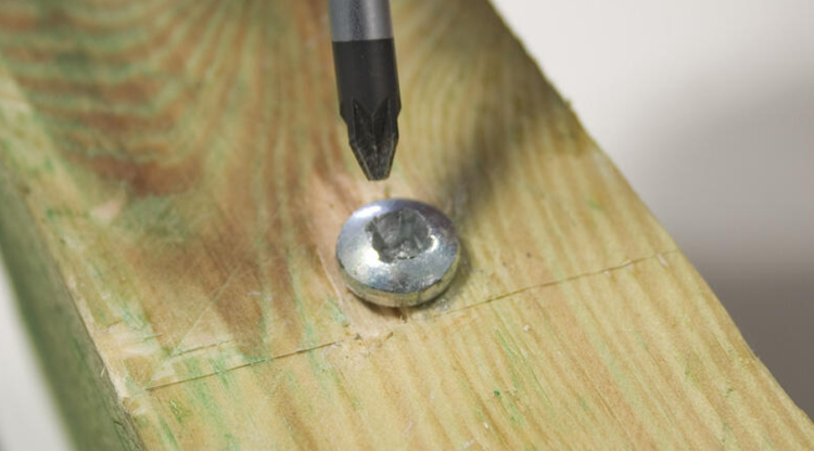 Schraube wird mit Schraubendreher in Holzplatte gedreht