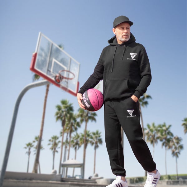 Mann mit schwarzem Trainingsanzug und Basketball vor einem Basketballkorb