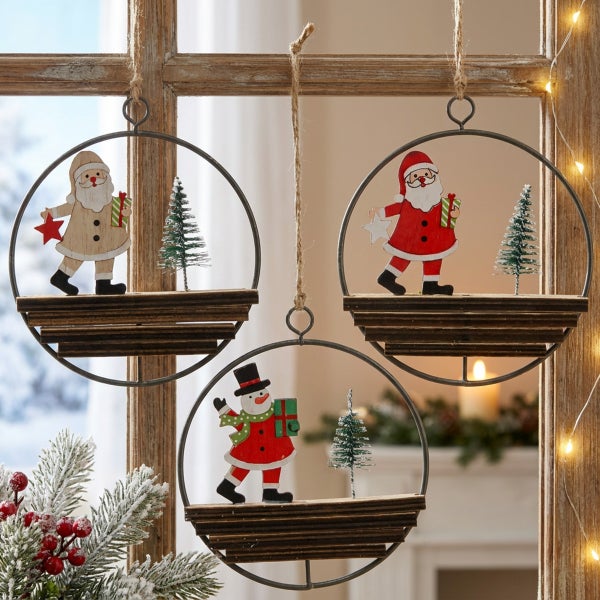 Drei hängende Weihnachtsdekorationen aus Holz und Metall mit Weihnachtsmann und Schneemann Figuren und kleinen künstlichen Tannenbäumen.