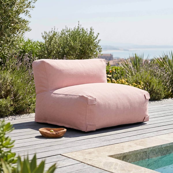 Rosa Outdoor-Lounge-Sessel auf einer Holzterrasse neben einem Pool, umgeben von Gartenpflanzen mit Küstenblick im Hintergrund.