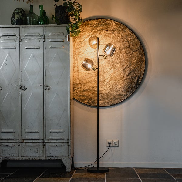 Moderne Stehlampe mit drei Glasschirmen im industriellen Stil neben einem Metallschrank und einer runden Wanddekoration.