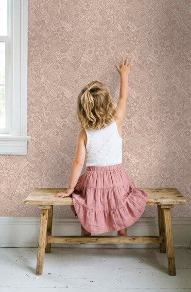 Tapete mit floralem Paisley-Muster an einer Wand hinter einem Kind, das auf einer Holzbank sitzt.