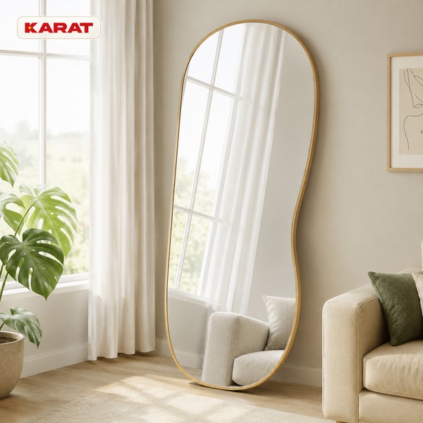 Großer, organisch geformter Ganzkörperspiegel mit Holzrahmen in einem Wohnzimmer neben einem Fenster und einer Pflanze. Karat Logo.