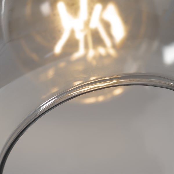 Nahaufnahme eines transparenten Glasschirms einer Lampe mit sichtbarem, leuchtendem Leuchtmittel im Hintergrund.