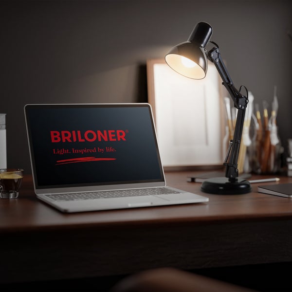 Schwarze verstellbare Schreibtischlampe auf einem Holztisch neben einem Laptop mit dem Briloner Logo in einem organisierten Arbeitsbereich.