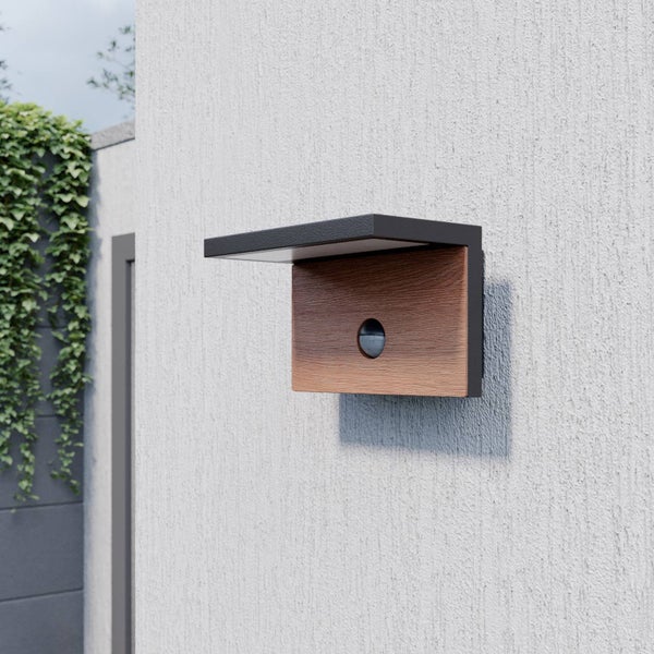 Moderne Außenwandleuchte mit Bewegungsmelder und Frontpaneel in Holzoptik an einer strukturierten Wand.