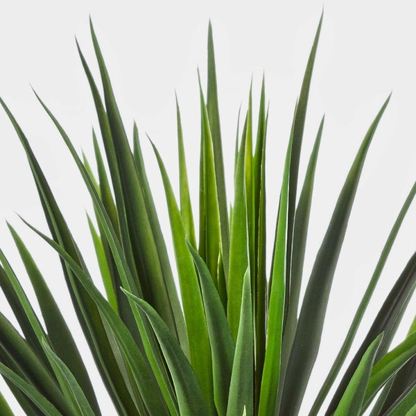 Künstliche Pflanze Yucca im schwarzen Topf, Detailansicht von Stamm und langen grünen Blättern.