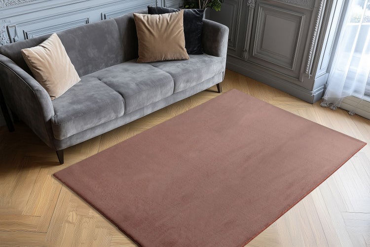 Ein unifarbener Wohnzimmerteppich in einem modernen Wohnraum mit Sofa und Fischgrätparkettboden.