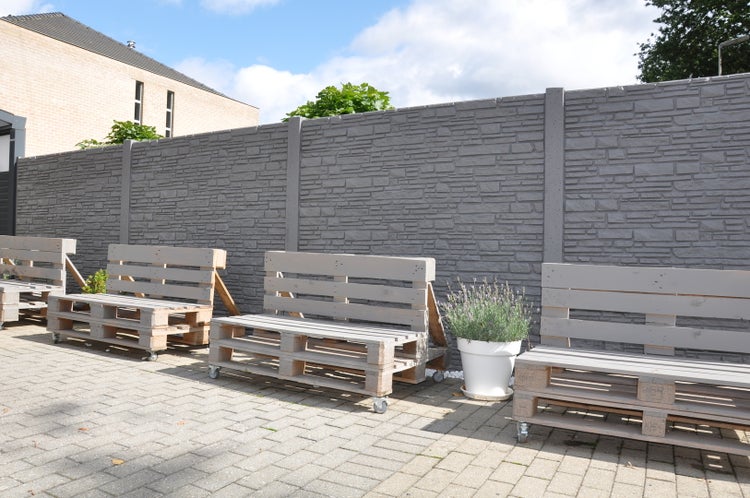 Gartenansicht mit Steinzaun und Palettenbänken