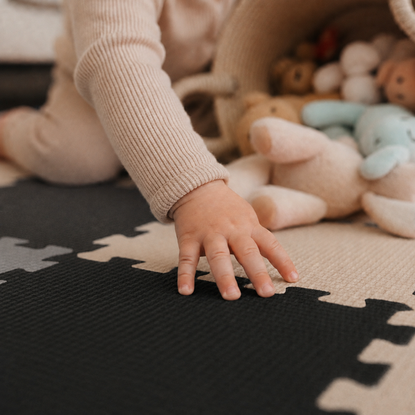 Ein Kleinkind spielt auf einer gepuzzelten Spielmatte aus Schaumstoff mit Plüschtieren in einem Korb.