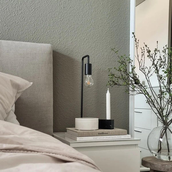 Schlafzimmer Szene mit Nachttischlampe, Kerze und Dekoration auf einem Nachttisch neben einem Bett