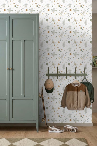 Helles Kinderzimmer mit Weltraum-Tapete, Schrank, Wandgarderobe mit Kleidung und einem Skateboard auf Holzfußboden.