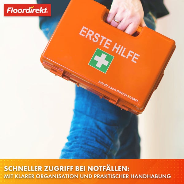 Person hält einen Erste-Hilfe-Koffer nach DIN 13157:2021.