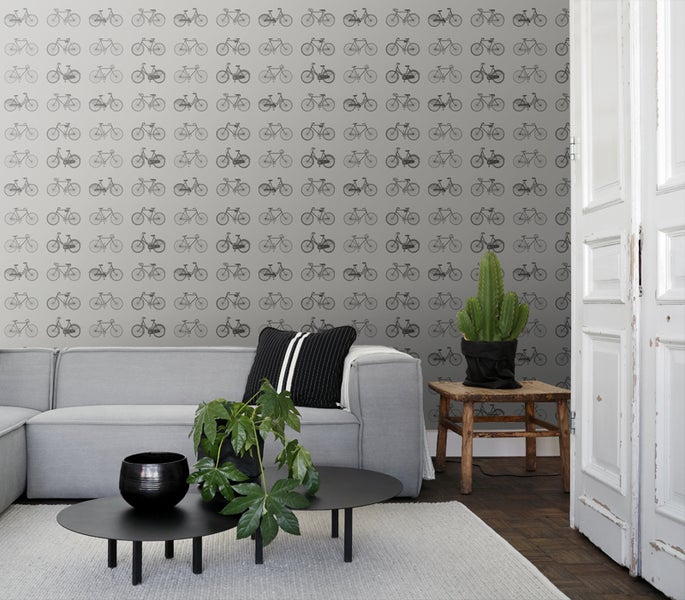 Wohnzimmer mit grauer Tapete mit Fahrradmuster, grauer Couch, Couchtisch und Zimmerpflanzen.