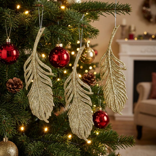 Drei glitzernde Weihnachtsbaumschmuck Anhänger in Federform hängen an einem geschmückten Tannenbaum mit Lichterkette und Weihnachtskugeln.