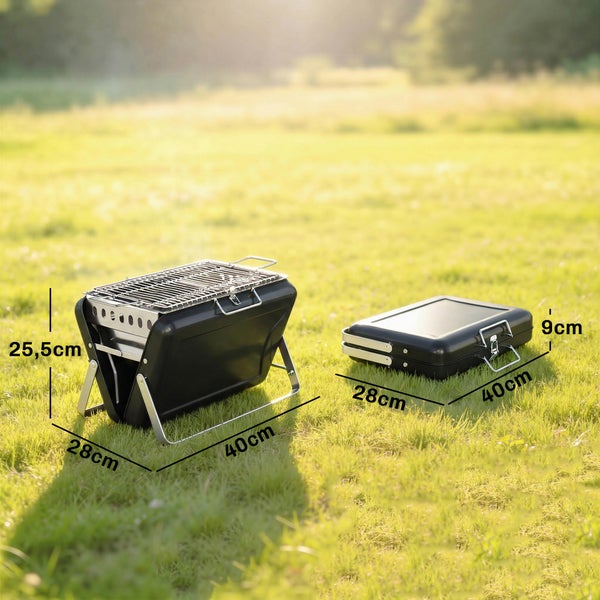 Tragbarer Holzkohlegrill, klappbar. Maße offen 25,5 x 28 x 40 Zentimeter. Maße geschlossen 9 x 28 x 40 Zentimeter. Auf einer Wiese.