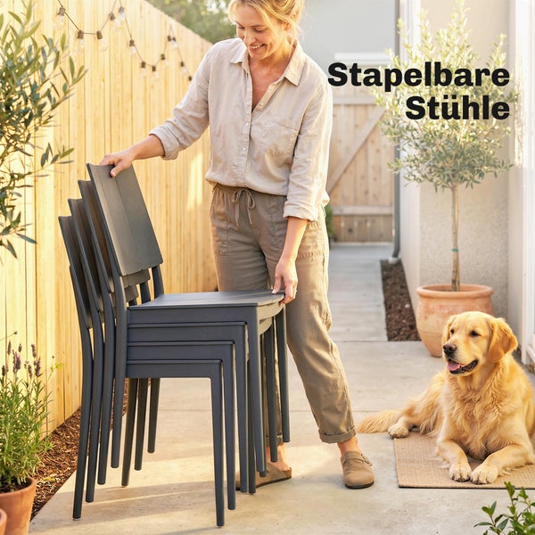 Eine Frau stapelt dunkelgraue Gartenstühle aus Kunststoff auf einer Terrasse mit Holzzaun und einem Hund.