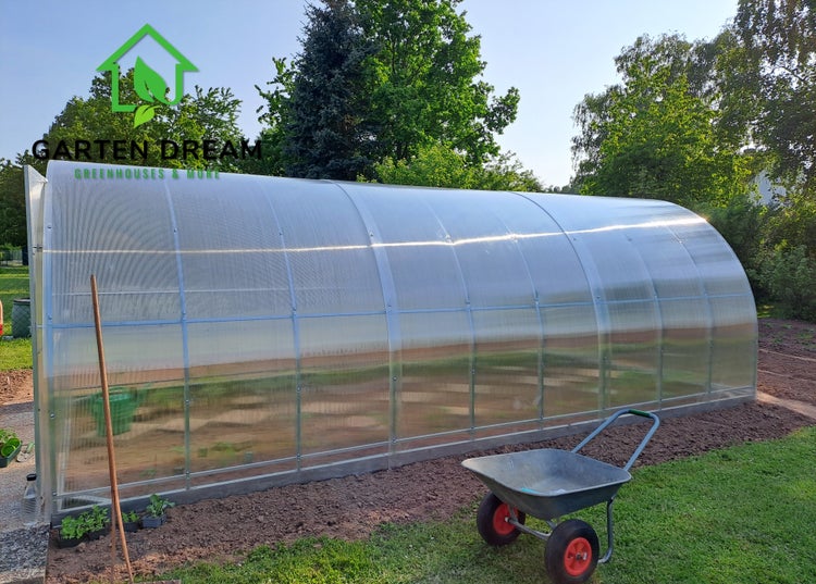 Gewächshausbogen im Garten mit Schubkarre und Gartenwerkzeug