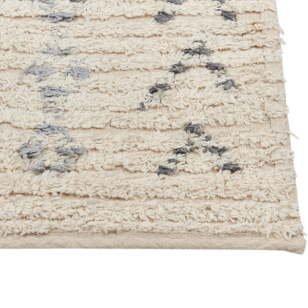 Detailaufnahme eines cremefarbenen Hochflor-Teppichs mit grauen Mustern und strukturierter Oberfläche sowie gewebter Kante.