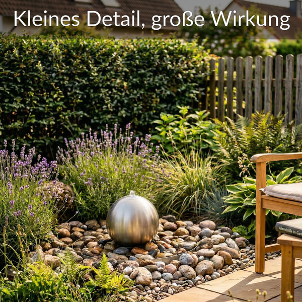Edelstahl-Kugelbrunnen in einem Garten mit Kieselsteinen, Lavendel und Farnen neben einem Holzstuhl.