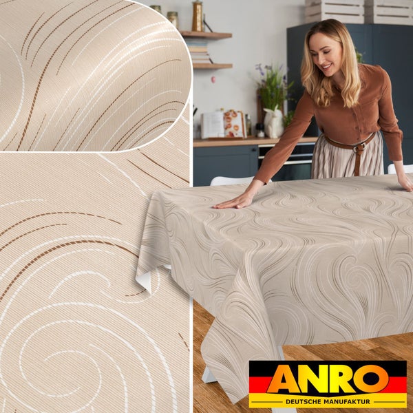 Frau legt gemusterte Tischdecke mit geschwungenem Linienmuster auf einen Tisch in einer hellen Küche. Inklusive ANRO Deutsche Manufaktur Logo.
